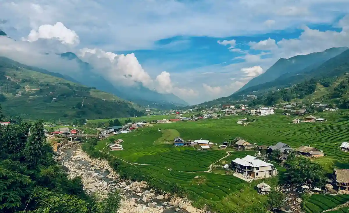 Wide green valley with stream, rice terraces and mountain village on the Classic Full-Day Valley Trek in Sa Pa